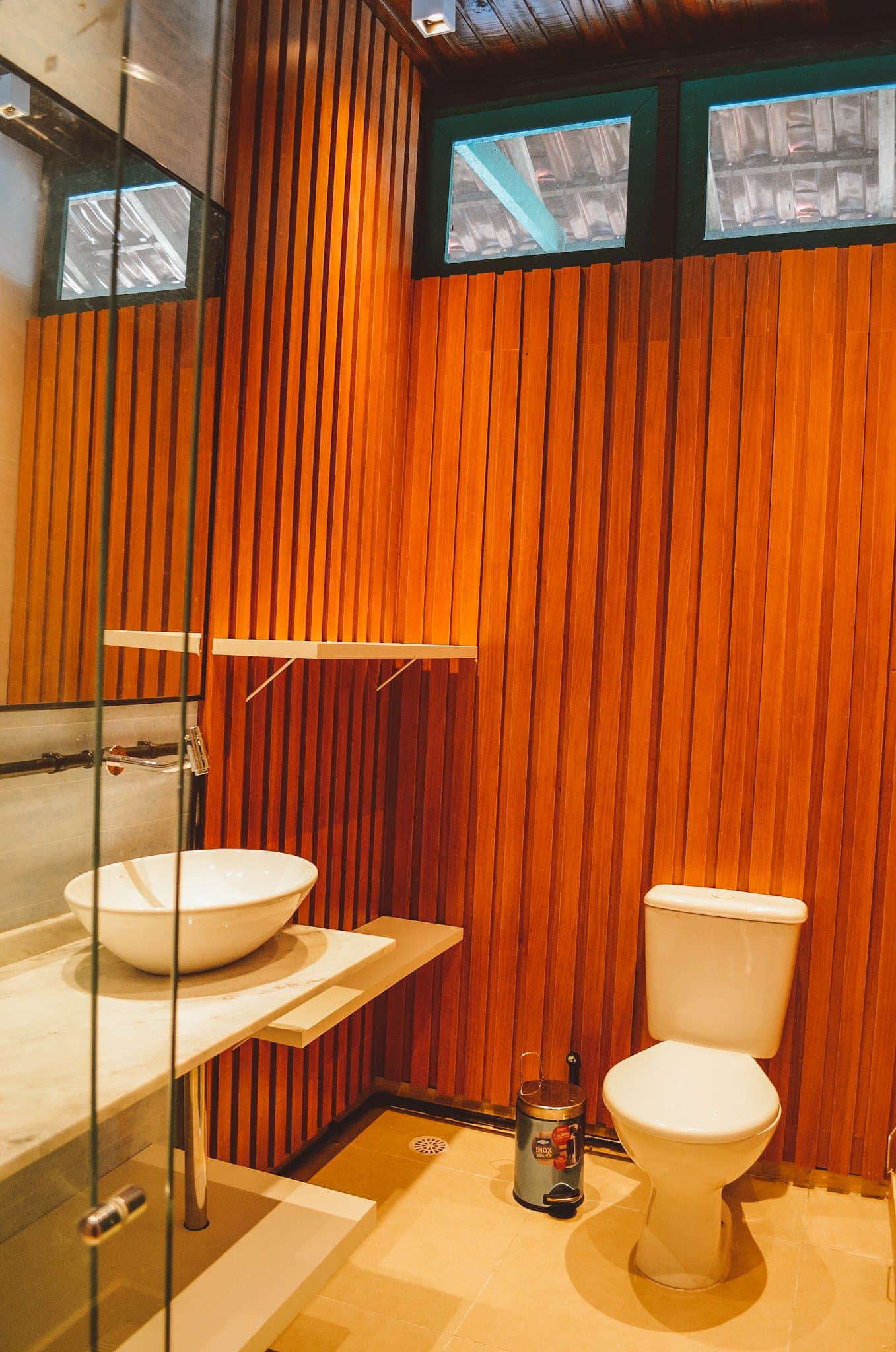 Warm hout, een echte wastafel, en genoeg licht om je zonnebrand te vinden. Privébadkamer van de Uakari Lodge tijdens een amazon rainforest ecolodge trip in brazil, met warme houten lamellenwanden, een witte opzetwastafel op een marmeren blad en glasblokramen hoog in de muur