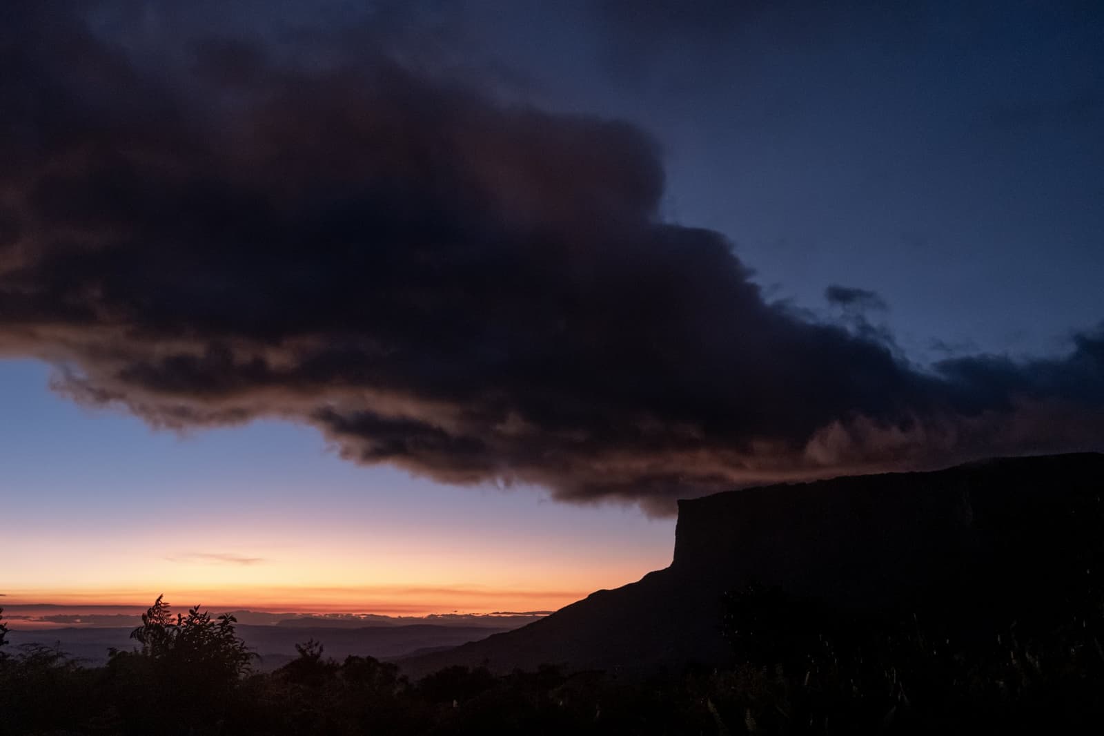 Storm in aantocht of niet, de horizon weet elke avond te imponeren. Dieporanje en rode zonsonderganggloed aan de horizon onder een grote donkere onweerswolk, met de silhouet van een tepui-tafelberg rechts zichtbaar tijdens een Mount Roraima-expeditie
