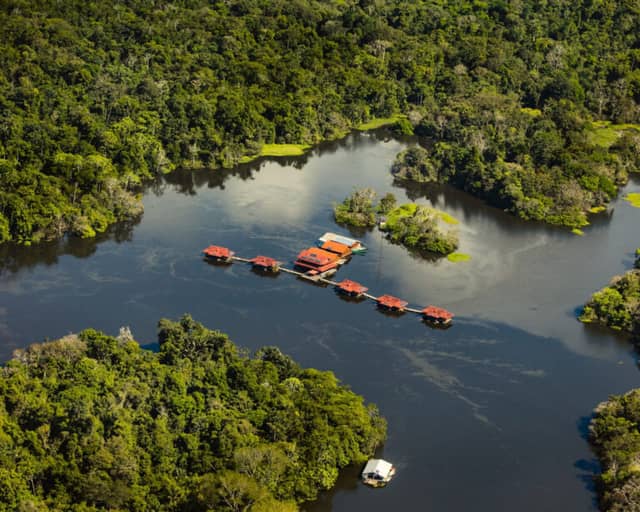 Aerial view of Uakari Floating Lodge, its red-roofed cabins lined along a walkway on the lake inside the Mamirauá Reserve