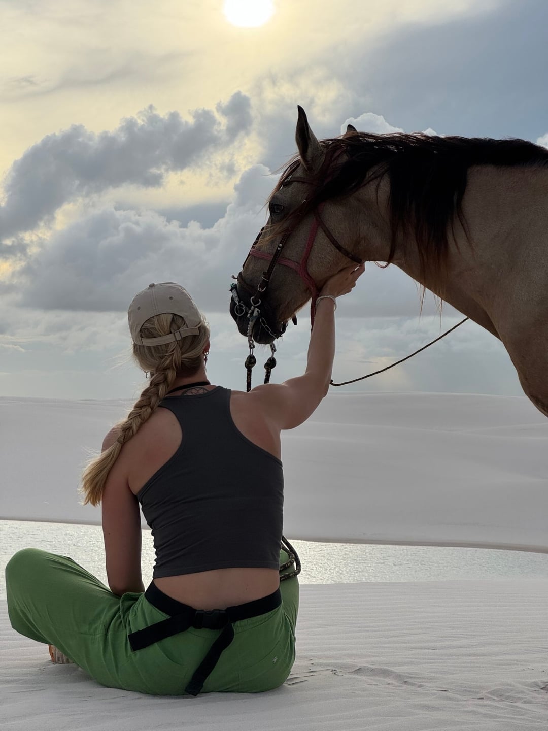 A rider in a cap pauses to stroke her horse's nose on the white dunes of Lençóis Maranhenses at sunset. A rider in a cap pauses to stroke her horse's nose on the white dunes of Lençóis Maranhenses at sunset.