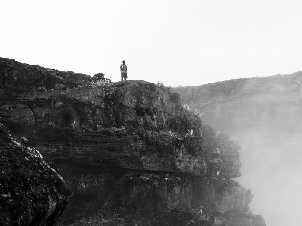 Un escursionista su una falesia avvolta dalla nebbia in cima al Monte Roraima, in bianco e nero Un escursionista su una falesia avvolta dalla nebbia in cima al Monte Roraima, in bianco e nero