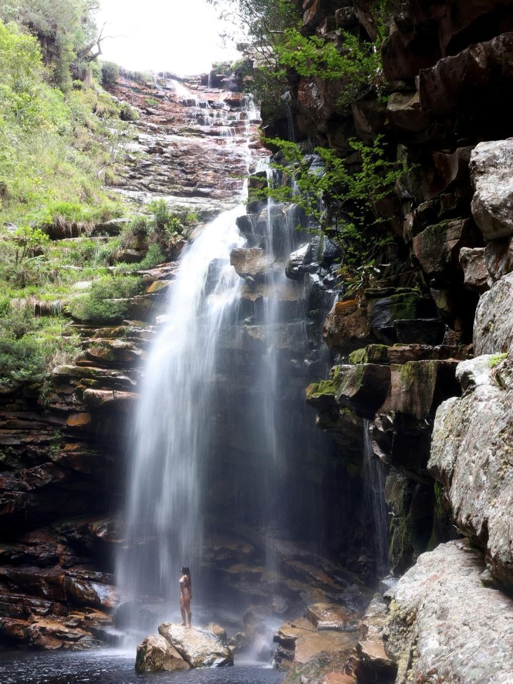 Una persona de pie sobre una roca al pie de una cascada alta en el Vale do Pati, en la Chapada Diamantina, Brasil. Una persona de pie sobre una roca al pie de una cascada alta en el Vale do Pati, en la Chapada Diamantina, Brasil.