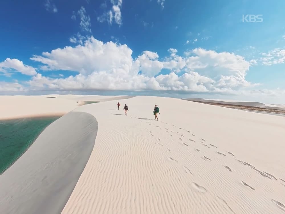 Photo: KBS Trekkers walking along a white sand dune next to a turquoise lagoon in Lençóis Maranhenses